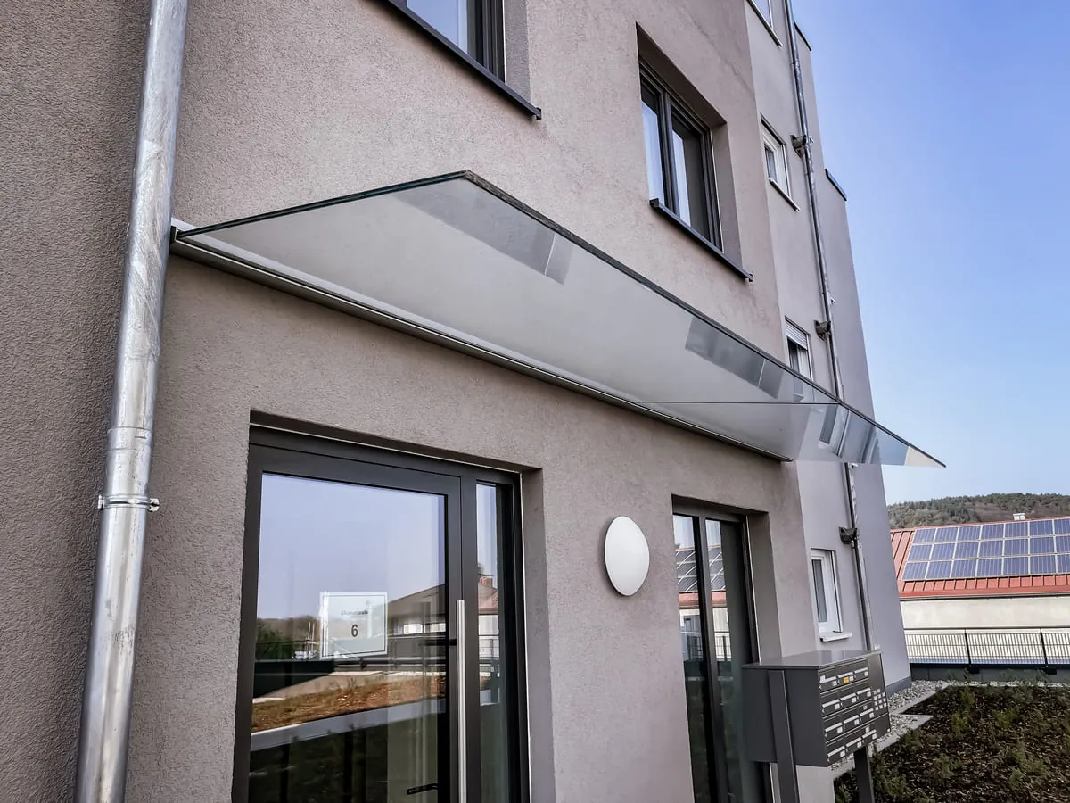 Glasvordach mit Wandmontage am Eingang eines Mehrfamilienhauses