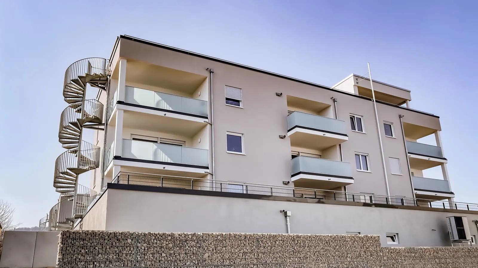 Verzinkte Spindeltreppe am Mehrfamilienhaus mit Balkongeländer aus Glas